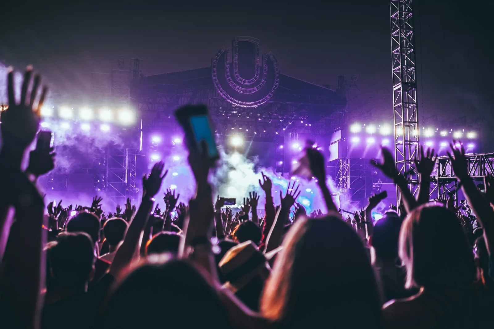 A crowd with their hands raised in front of a brightly lit stage