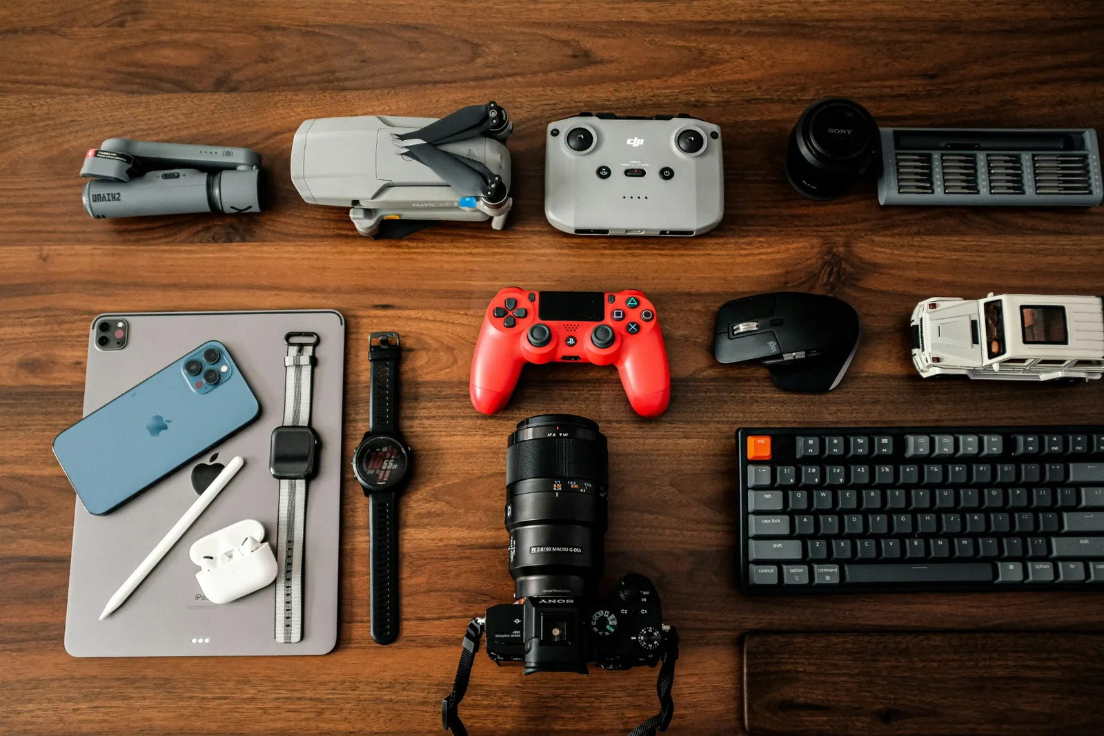 A camera, keyboard, game controller and phone laid out on a wooden desk
