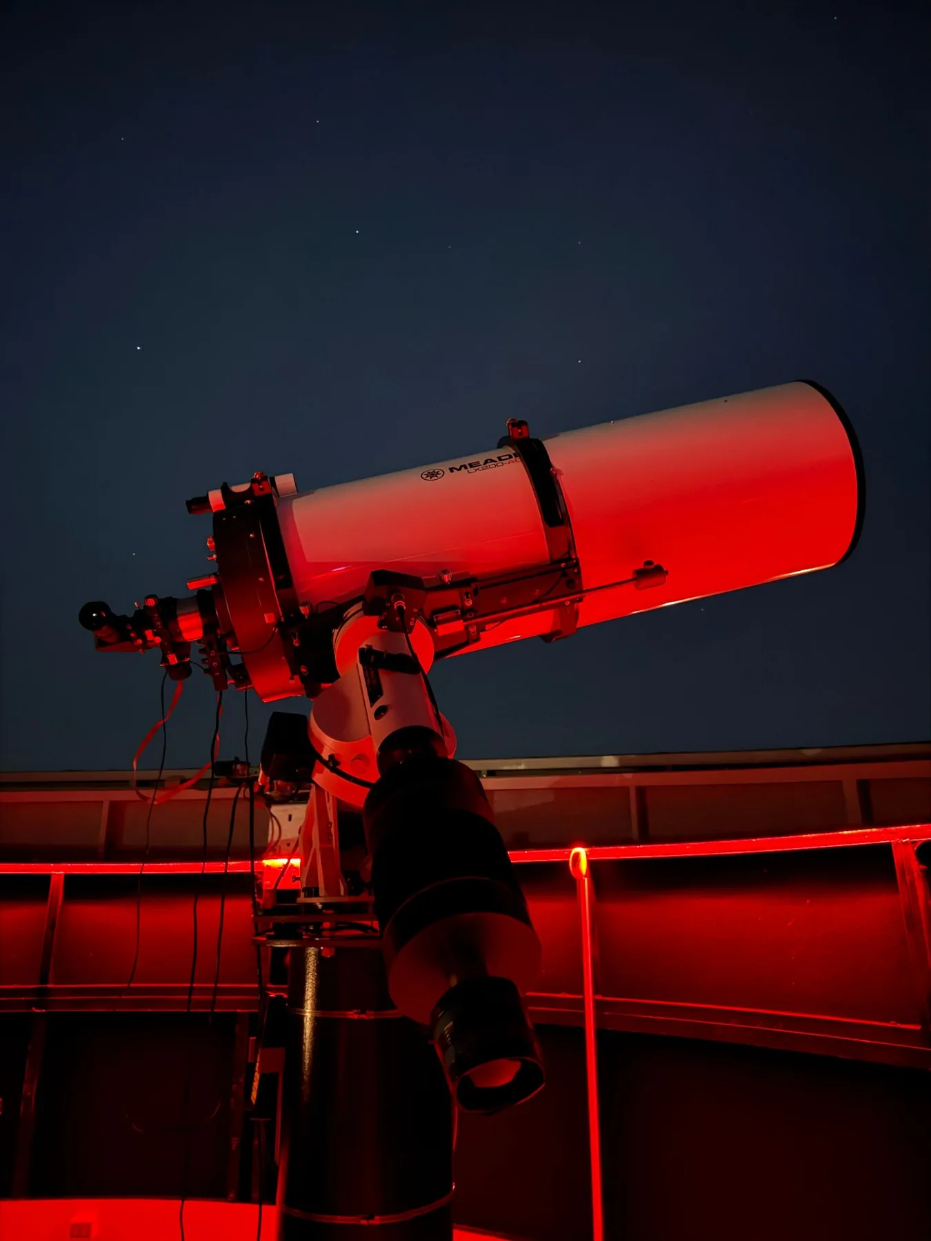 A large telescope pointed at the night sky inside a red-lit observatory