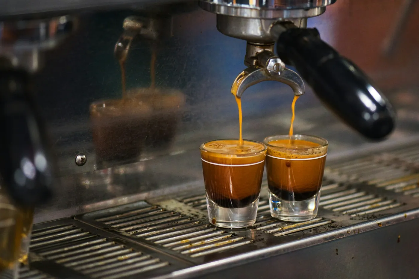 An espresso machine pouring coffee into two small glasses