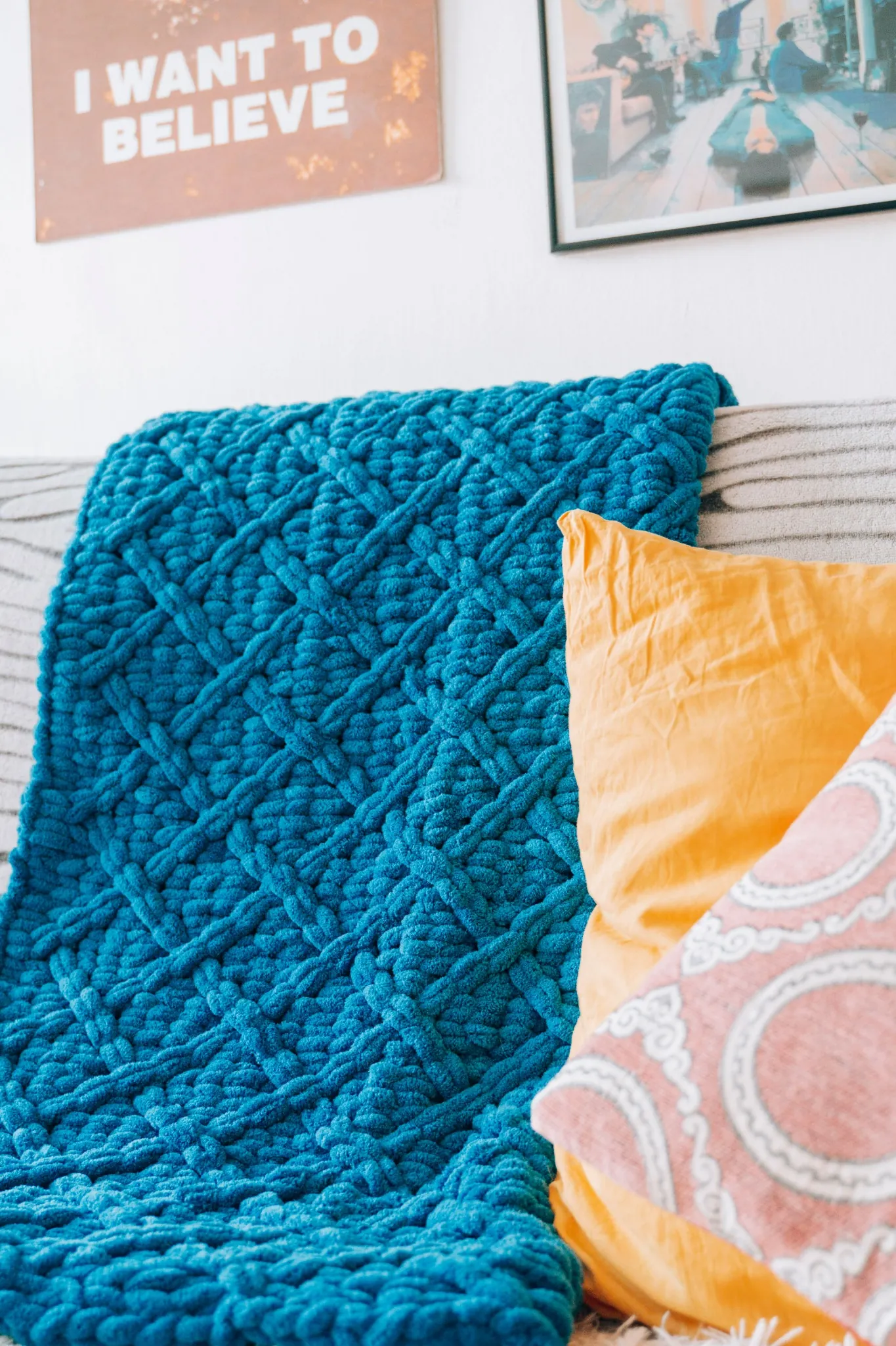 A chunky teal knitted throw draped over a sofa with colourful cushions