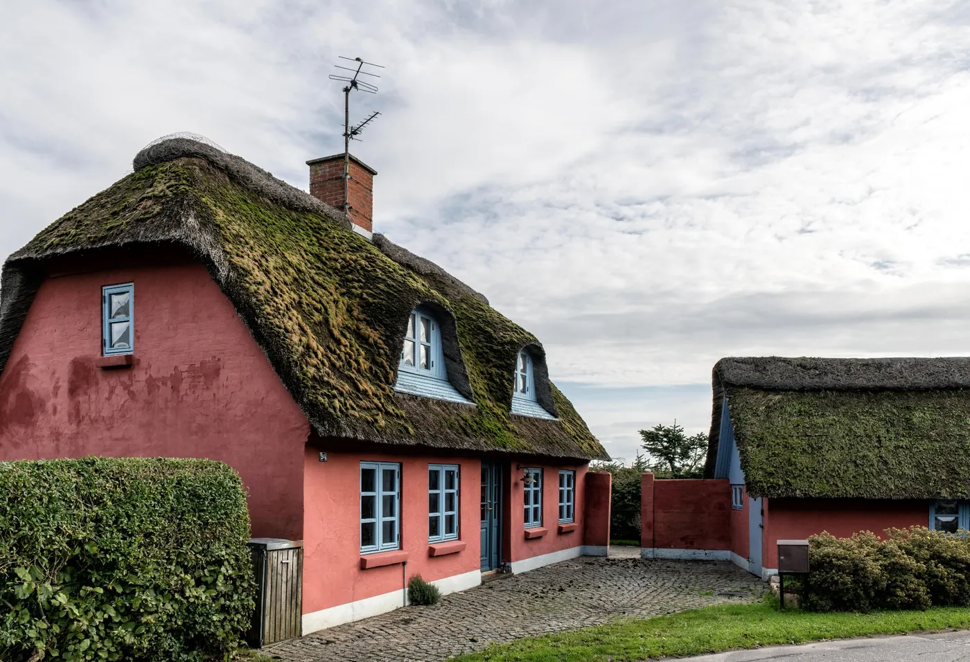A thatched countryside cottage with a pink exterior and blue window frames