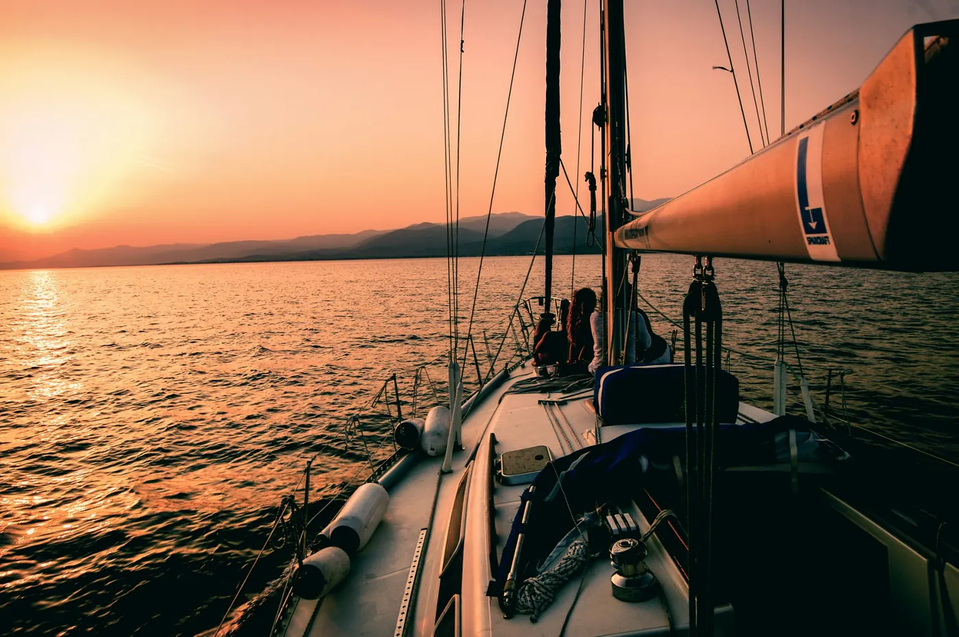 People seated on a sailboat at sunset, with the sun low over the water