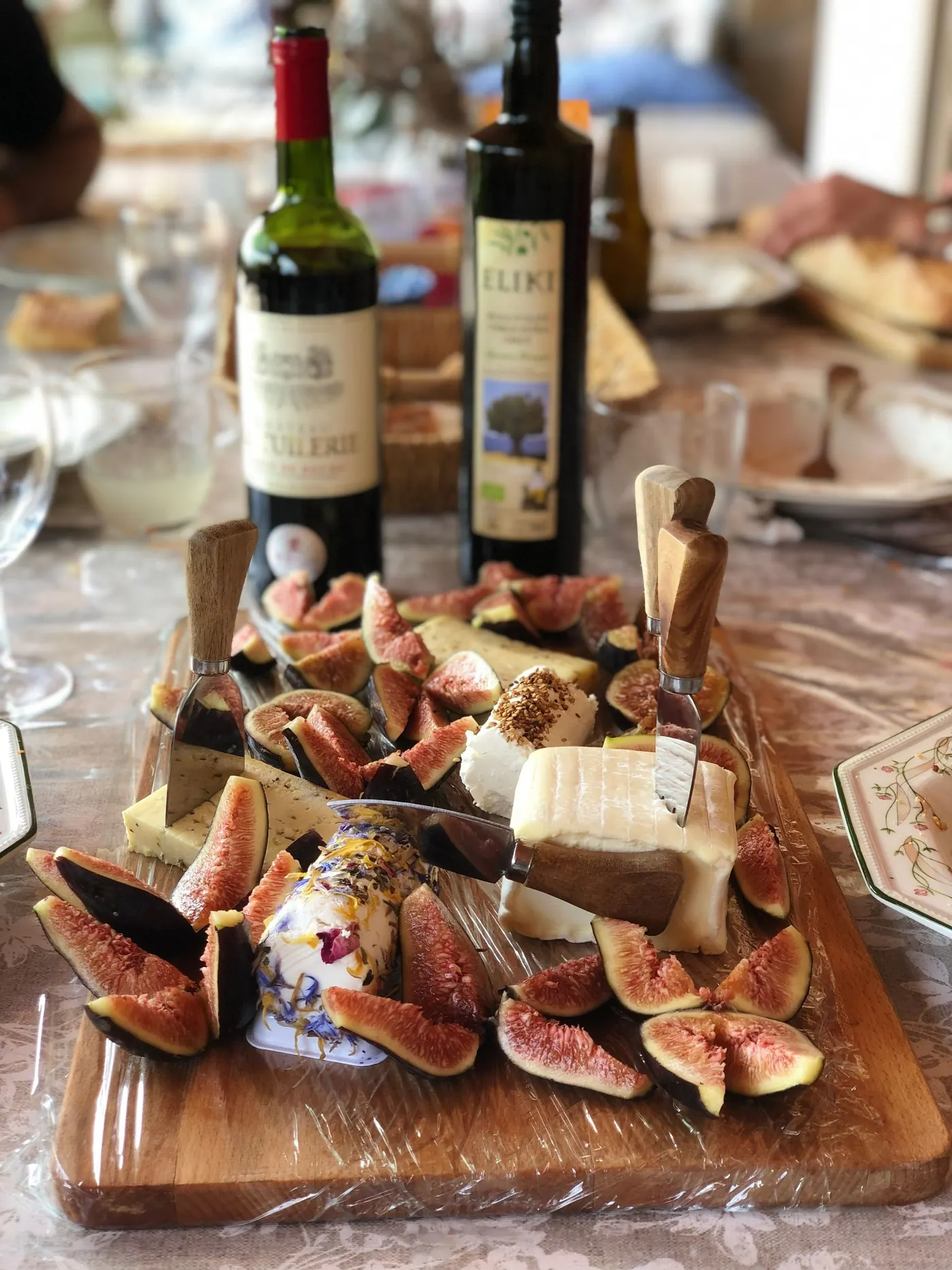 A wooden board with cheese, figs and bread on a dining table